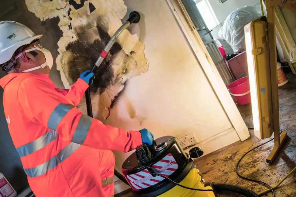 Technician in protective gear cleaning soot and charred materials from a fire-damaged wall, illustrating fire damage restoration processes.