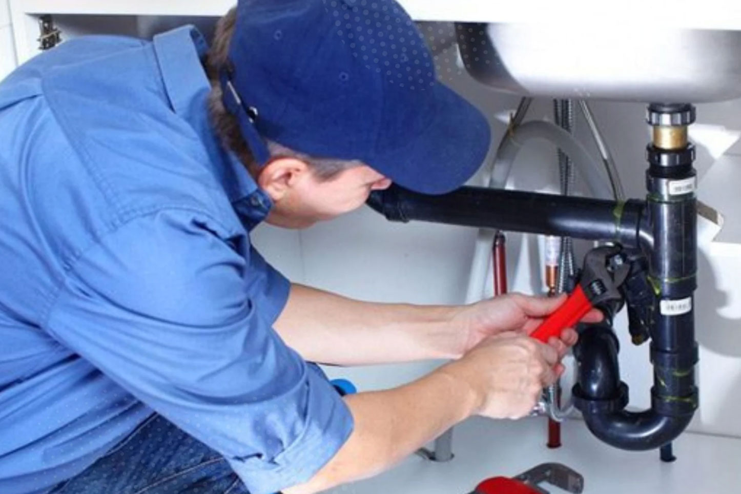 Plumber fixing a pipe under a sink that has corroded over time in a house causing water damage.